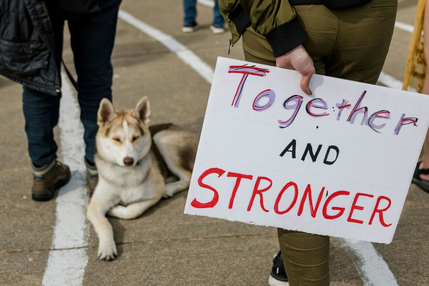 sign that says together and strong, husky dog in the background and two people's legs
